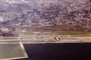 Aerial shot of the Nike missile base along Milwaukee's lakeshore. The city's landscape is in the background showing buildings, highways, and a long river on the left.