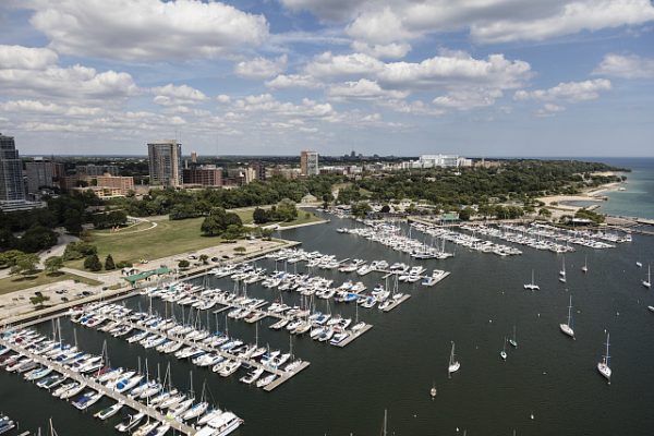 Aerial shot of rows of boats moored in the marina in Lake Michigan. In the background of this image is the wide landscape of Milwaukee against the blue sky.