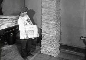 A young Kruyer Polski newspaper carries stands next to a stack of the 40th anniversary edition of the paper in 1928. The paper began in 1888 and was published until 1962.