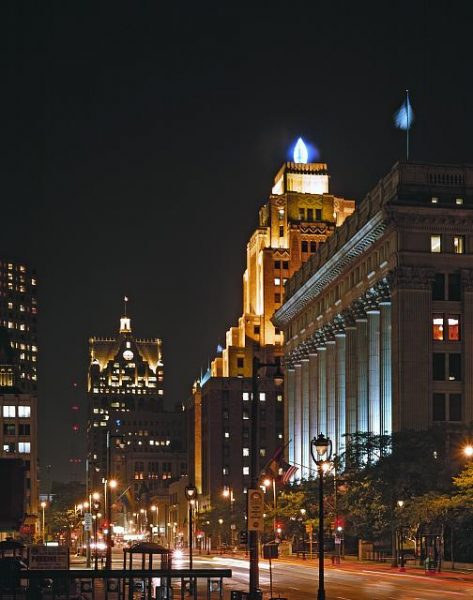 Night view of a street in Milwaukee showing blue light shining from the weather beacon in the form of a flame over the Wisconsin Gas Company building.