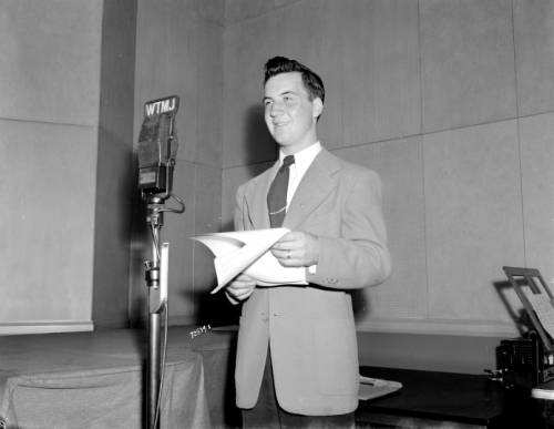 A radio announcer stands behind a microphone during a broadcast of the WTJM radio program called "Rumpus Room" in 1945. The program featured advertisements for local retailers like Boston Store.