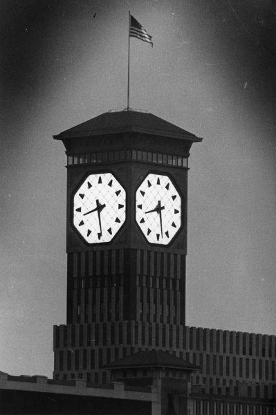 Close up of the Allen-Bradley Clock Tower, in grayscale. The analogue clock glows, displaying the time at 08.30. The Stars and Stripes flag waves above the top of the tower.