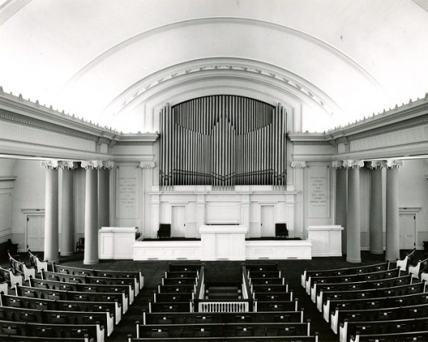 Grayscale image of the former First Church of Christ's interior showing its large nave with an altar and organ pipes in the center background and rows of pews under a vaulted ceiling.