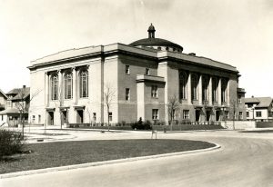 Sepia-colored long shot of the former Third Christian Science Church, facing slightly to the right. This image shows two sides of the building. The one on the left features three tall arched regularly spaced windows. The one on the right has five identical arched windows above and three entrance doors below. A dome structure adorns the top center of the flat roof.