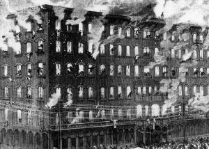 A drawing illustrates the dramatic scene of the Newhall House blaze rescue operation. Severe fire and clouds of smoke stream out of the hotel windows and roof. People seeking help stand on the hotel's arched windows. Some jump to the safety nets held by firefighters below. Other groups of firefighters carry ladders toward the hotel. On the farthest right, some climb a ladder attached to the building. A crowd appears around the Newhall House's entrance. A throng of people stands in the foreground, watching the rescue operation.