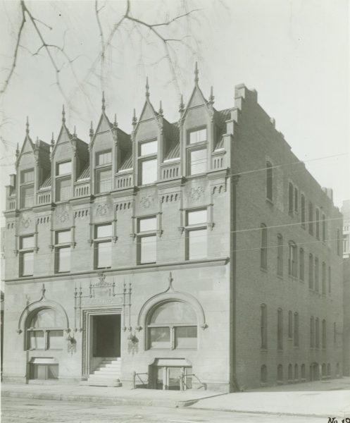Sepia-colored of the Johnston Emergency Hospital facade by a street. The structure has five dormer windows. The facade's second floor has five rectangular windows. The ground floor features arched structures adorning the windows beneath that flank the central entrance.