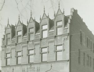 Sepia-colored of the Johnston Emergency Hospital facade by a street. The structure has five dormer windows. The facade's second floor has five rectangular windows. The ground floor features arched structures adorning the windows beneath that flank the central entrance.