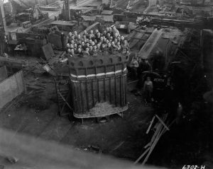 Grayscale high-angle shot of 52 men standing inside a massive dipper for a Bucyrus-Erie 950-B stripping shovel. Appearing in the background are abundant kinds of equipment filling the plant's interior.