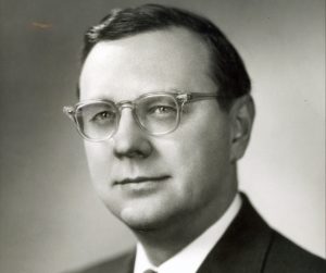 Grayscale headshot of Frank Zeidler from the chest up in formal attire and glasses. His eyes and body face slightly to the left.