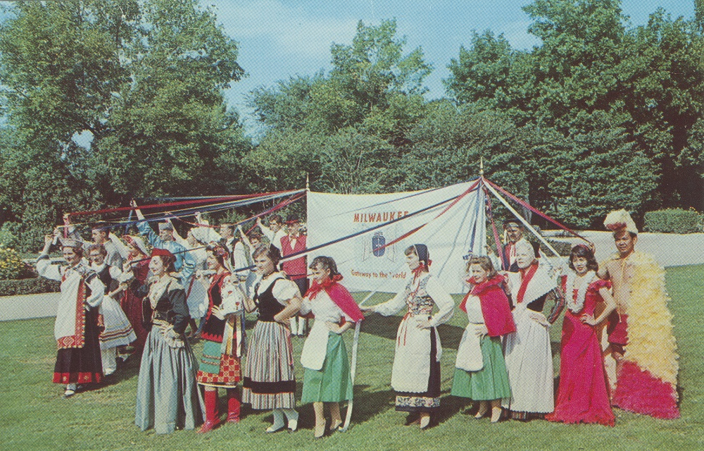 Men and women dressed in traditional costumes stand outside holding a banner during the Holiday Folk Fair. 