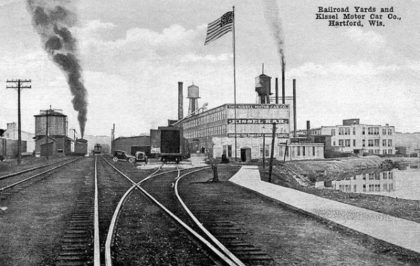 Black-and-white postcard featuring a railroad yard and the Kissel Motor Car Company building in Hartford. Long and crisscrossing railway track lines dominate the left portion of the postcard.