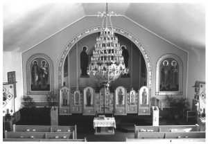 Elevated view of the interior of St. Michael's Ukrainian Catholic Church. Various biblical-themed ornaments embellish the interior. The iconostasis appears in the image's center. The pews are visible. A large chandelier is above the aisle.