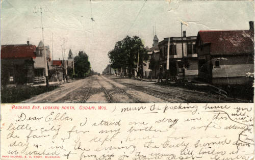 Vintage postcard of Packard Avenue. The image is divided horizontally with a panoramic view of the street on the upper portion and a handwritten letter to someone named Ellen on the bottom. The upper image shows a long wide street separating the buildings, with utility poles and streetcar wires adjacent to and above the road.