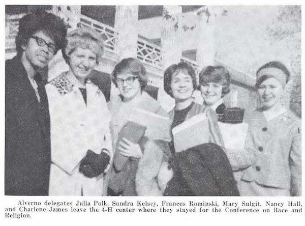 Alverno college students Julia Polk, Sandra Kelsey, Frances Rominski, Mary Sulgit, Nancy Hall, and Charlene James, smiling in their Fall outfits. Some wear glasses and coats, some hold books, as they pose in front of a building.