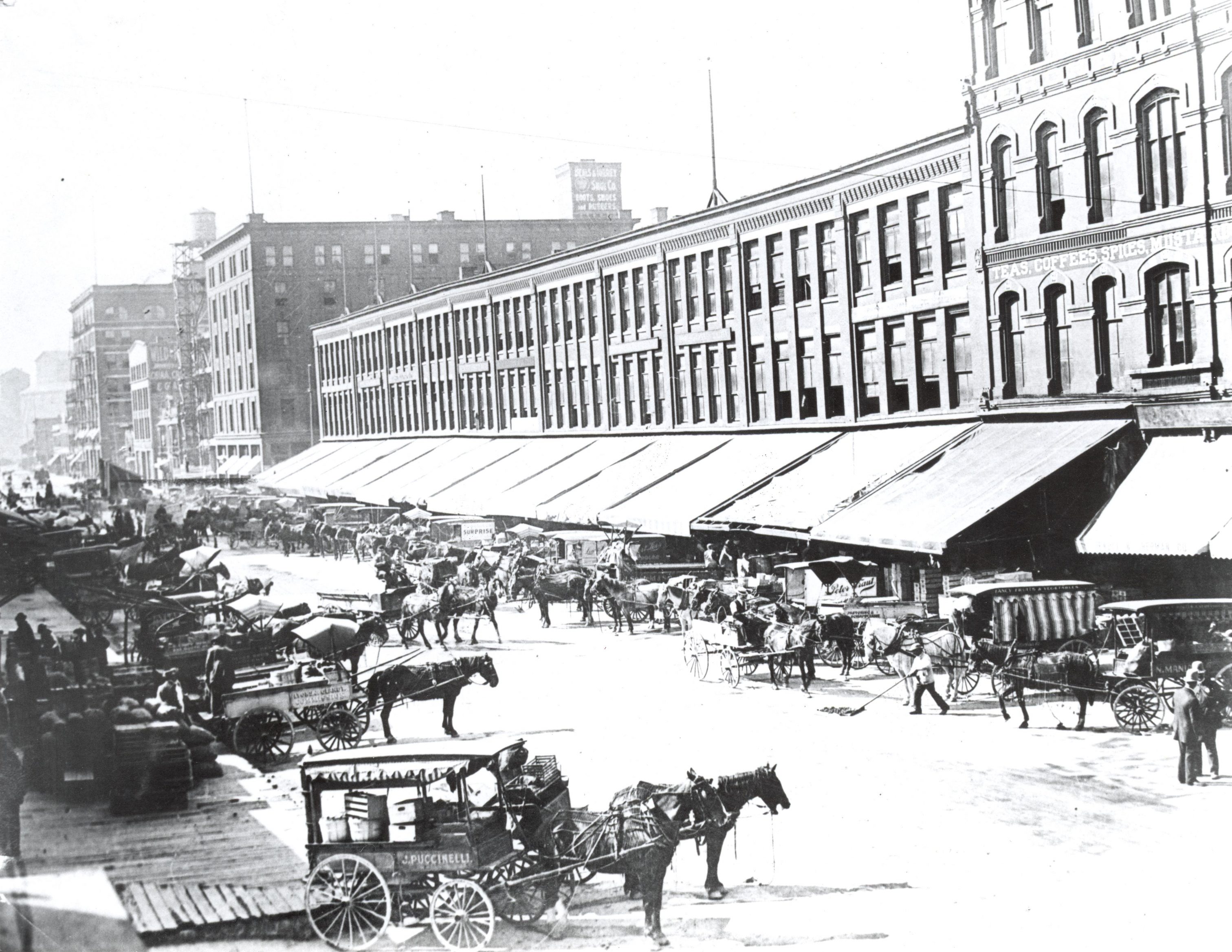 Horse-drawn carts full of produce line Commission Row on Broadway Street. 