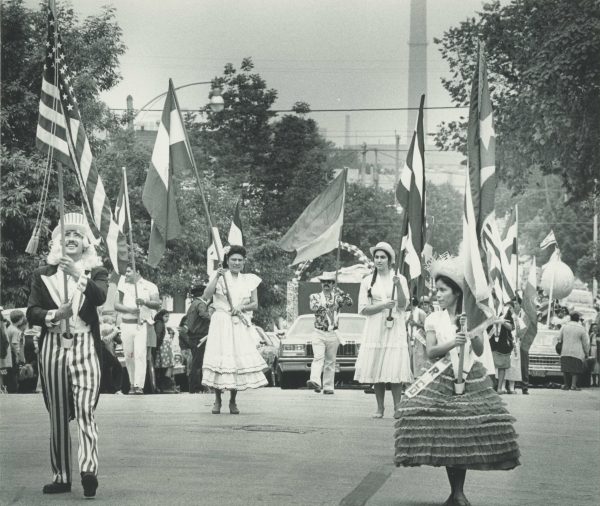 Men and women wearing costumes and carrying flags parade down the street at part of Mexican Fiesta in 1984.
