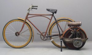 Wide shot of a bicycle facing left with a Briggs & Stratton 1920 Motorwheel engine mounted to its rear. The bike rims and fender set are in bright yellow; the frame is colored in light brown.