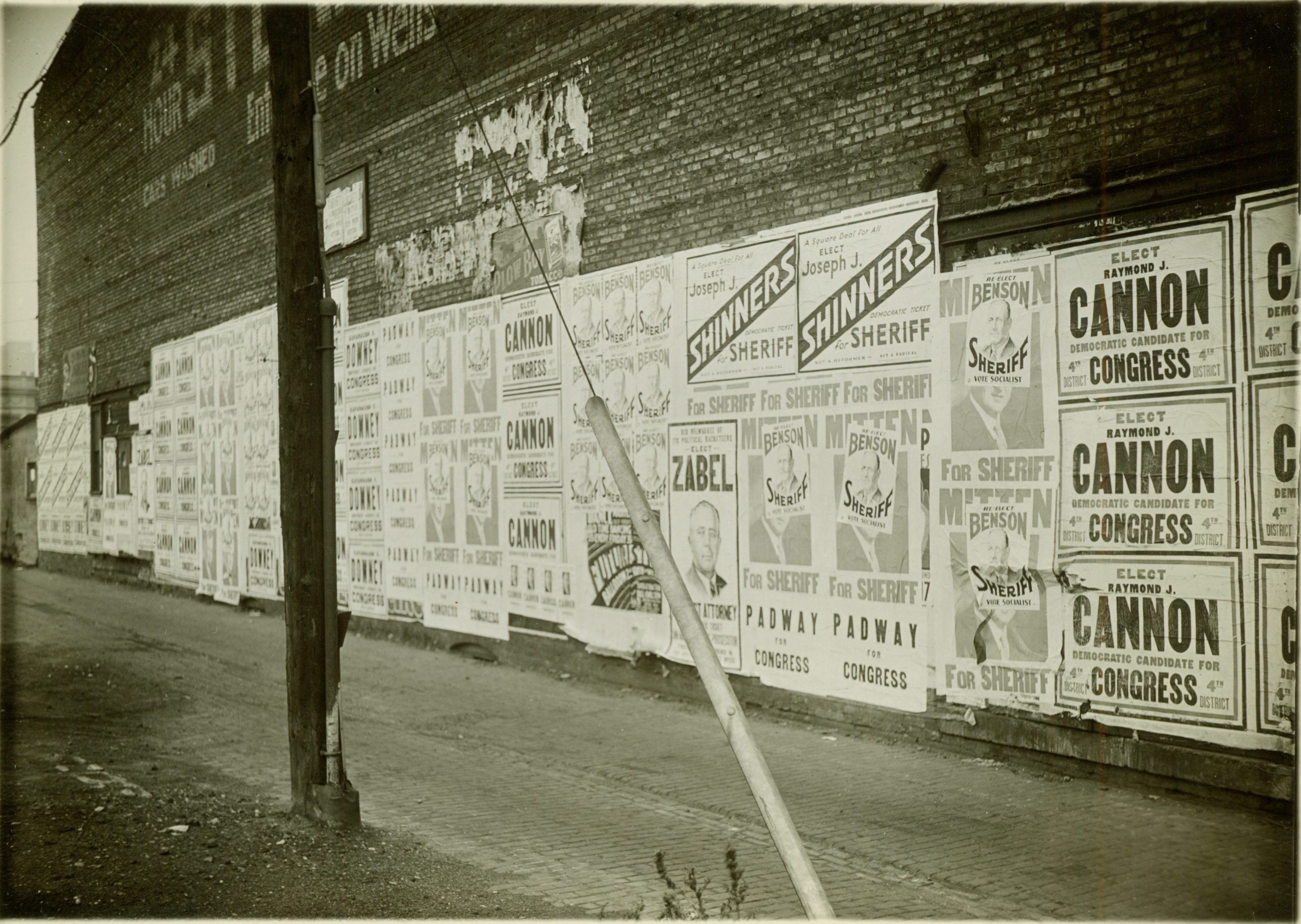 Campaign posters cover this brick wall on Wells Street in 1932. Candidates include Benson for Sheriff, Joseph Shinners for Sheriff, Raymond Cannon for Congress, and Zabel for District Attorney.