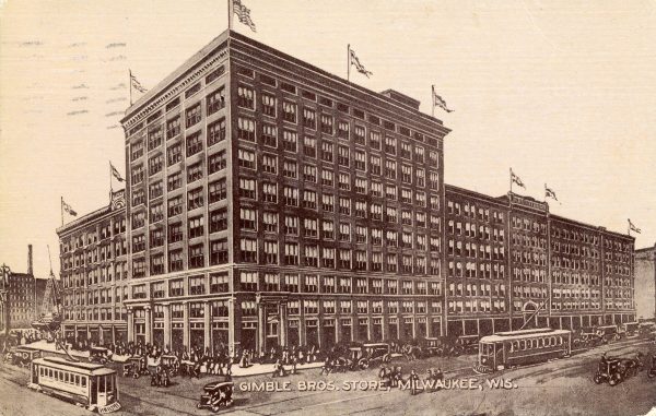 A vintage sepia drawing of Gimbel Bros. Department Store's facade and surrounding area. The tall building features flapping American flags perched around the roof and rows of windows in each of its stories. The department store takes up the entire block. The picture illustrates a busy day where crowds of people walk in front of the building next to a street where streetcars and vintage cars run.