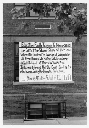 Grayscale photograph of a protest sign on the exterior wall of UWM's Kimberly Hall. The sign is titled "Education Faculty Telegram to Nixon-5-8-70." The text beneath the title announces the support for the student strike at UWM. The bottom part mentions the group that created the message. It reads "Students & Faculty-School of Ed.-UWM."