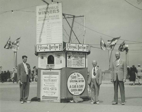 Three men stand beside a booth selling festival buttons for one dollar in 1941. The purchase of a button gave fairgoers admission to some of the festival's paid attractions and a chance to win a car. 