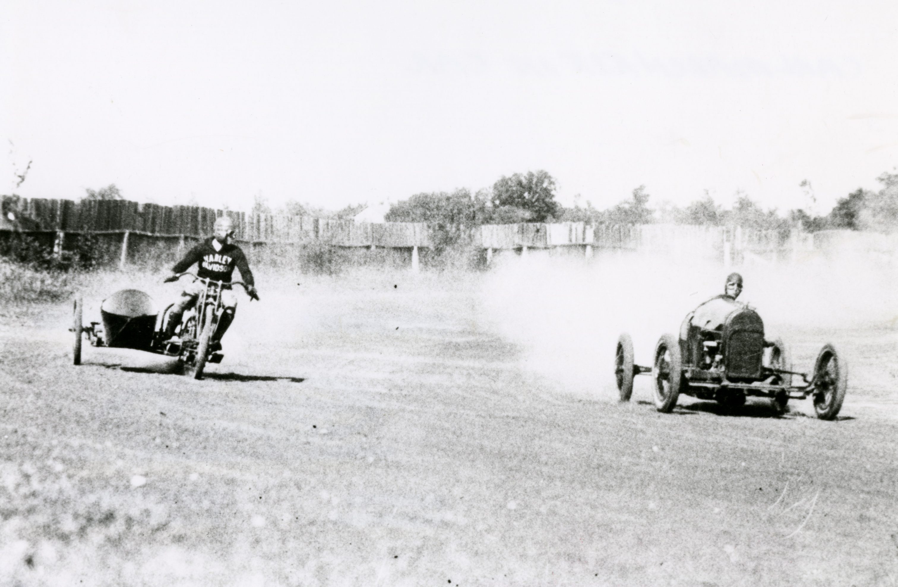 A man wearing a Harley Davidson jacket races an automobile driver at a track in Cedarburg some time in the 1920s.