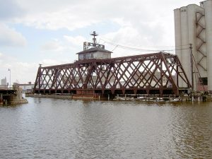 Long shot of the C&NW swing bridge stretching over the Milwaukee River in an open position. Parts of its metal structure are rusty.