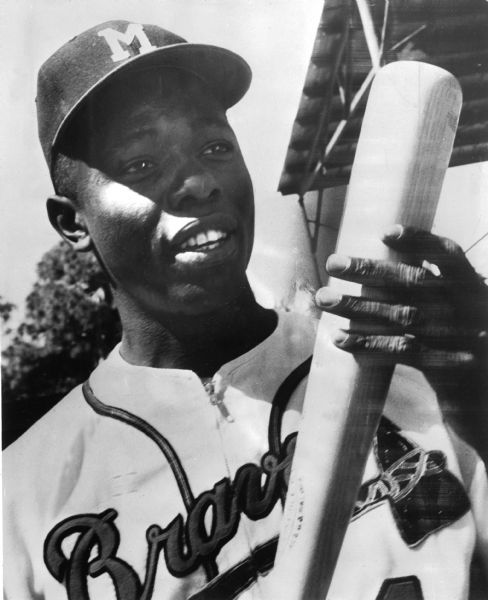 Hank Aaron holds a baseball bat while wearing his Milwaukee Braves uniform in this portrait. 