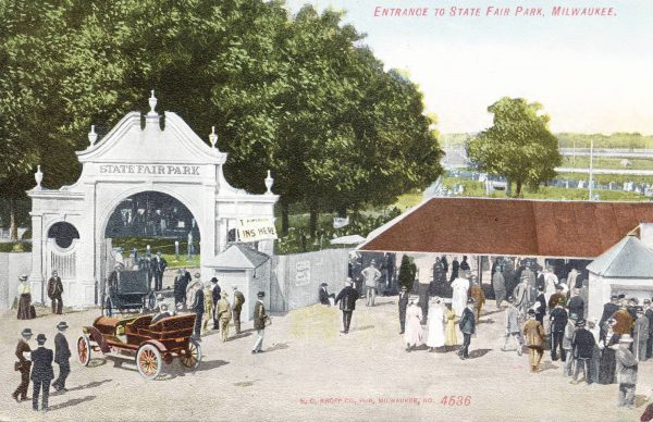A painted postcard illustrates a scene in the State Fair Park in West Allis. Automobiles and people appear around an ornate gate on the left. Groups of people gather on the right, next to a pavilion. Tall and lush green trees are in the background. The text at the top right reads, "Entrance to State Fair Park, Milwaukee."