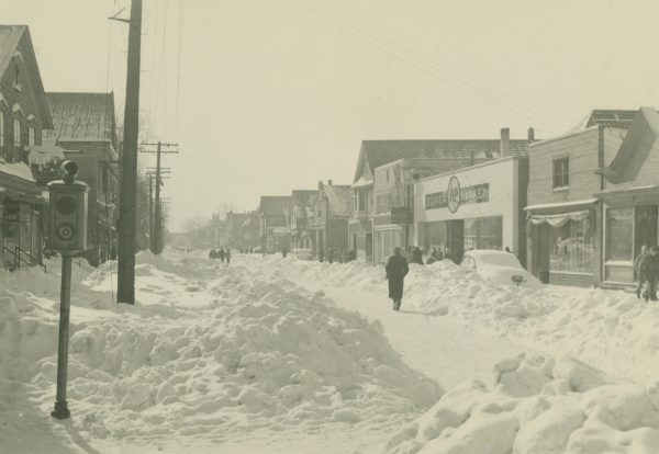 In 1947, a January blizzard brought sixteen inches of snowfall to Milwaukee and crippled the city. Pictured here the day after the storm, Teutonia Avenue is only partially plowed and snow drifts are piled high along the sidewalks. 