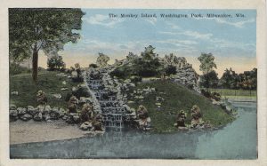 A painted postcard illustrates the Monkey Island at Washington Park. A group of monkey gathers on sloping green terrain with a small stair-step waterfall in the middle. The waterfall ends on a pond in the foreground.