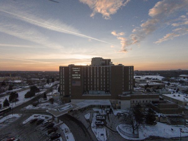 Aerial shot of Clement J. Zablocki VA Medical Center and its surrounding area partly covered by snow. The tall structure of the building stands out among other buildings in the neighborhood. Glowing in the distance is the name sign of the building that appears above a large American flag.