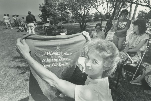 Cheryl Keenan, Milwaukee's representative in the National Organization for Women holds a shirt that reads "A woman's place is in the House...and the Senate" at the city's first women's festival in 1984.