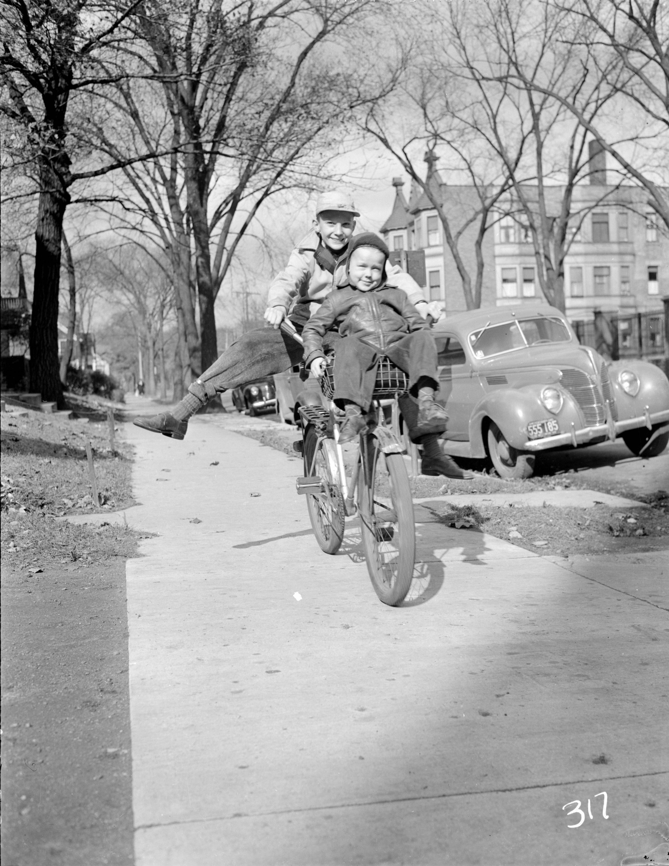 Two children share a bike as they ride down a Milwaukee sidewalk in October 1943. 