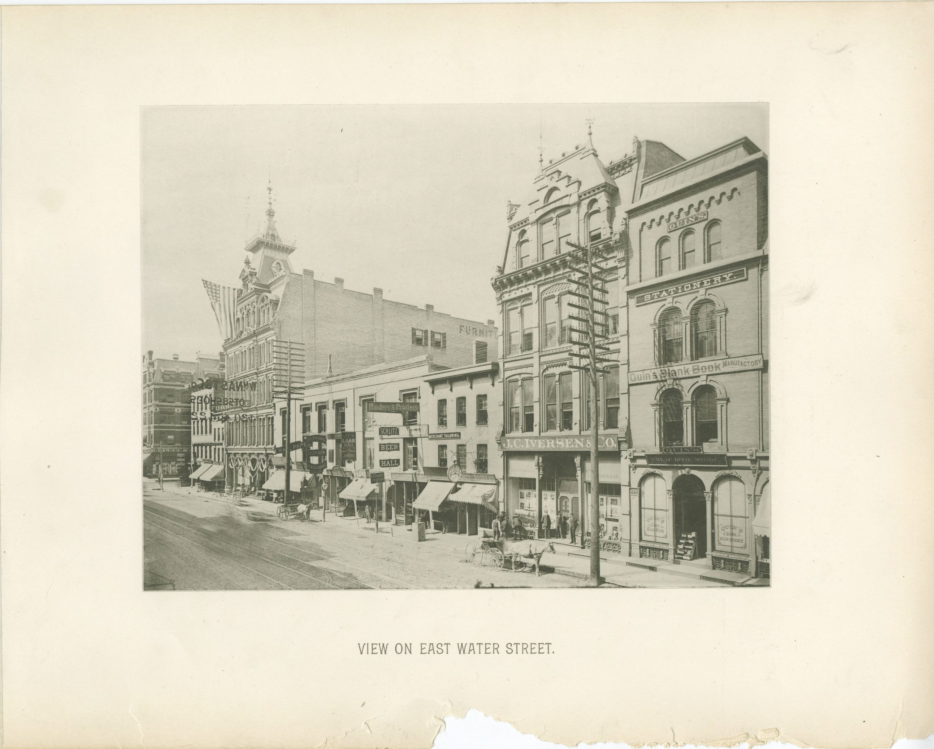 Taken in the 1880s, this block of Water Street between Wisconsin and Mason Streets features a wide variety of businesses, including a furniture store, saloon, tailor, printer and bindery, and bookstore.