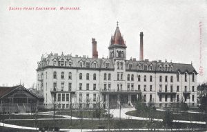 Postcard illustrating the Sacred Heart Sanitarium grand facade. The four-story building features a tower with a pyramidal roof on its central structure. A cross is set atop the red-colored roof.